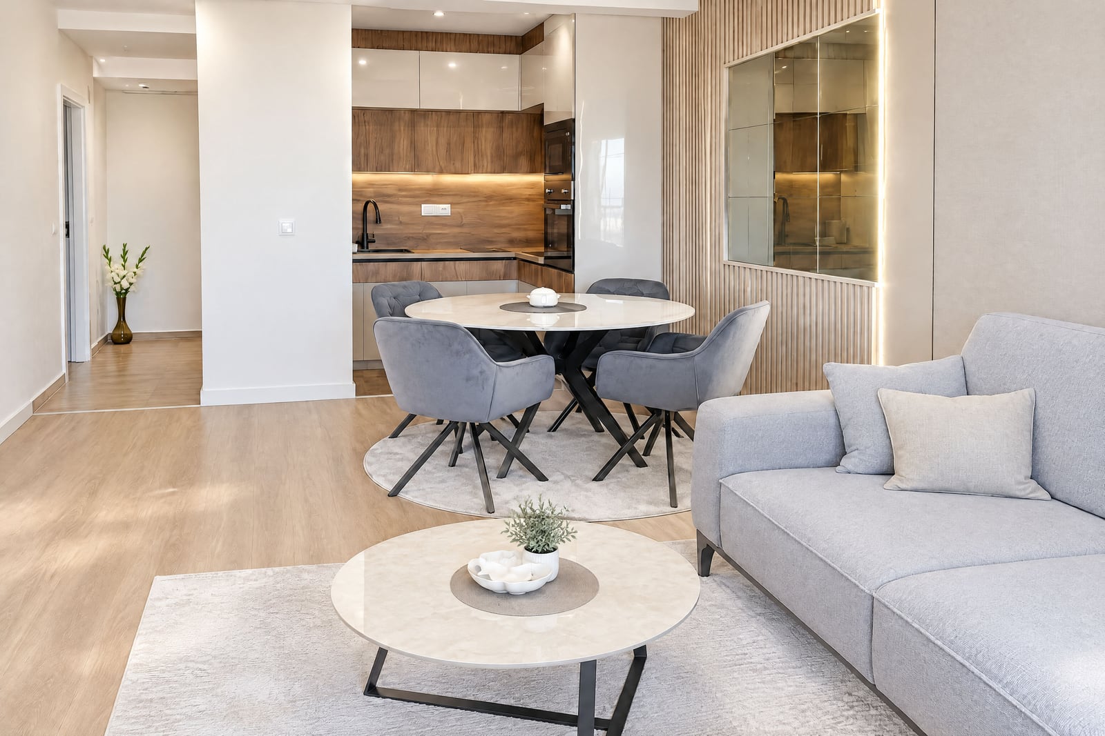 Modern living room with a grey sofa, round dining table, and visible kitchen in the background.