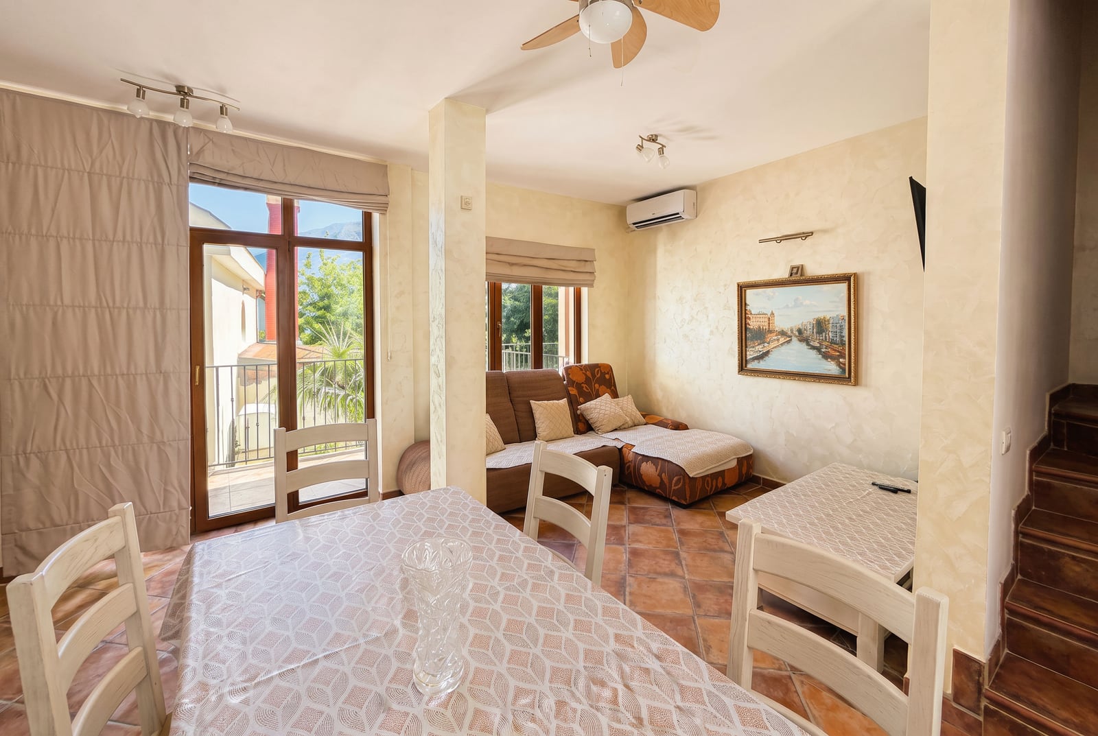 Living room featuring a dining table, brown sofa, ceiling fan, and glass door leading to a balcony.