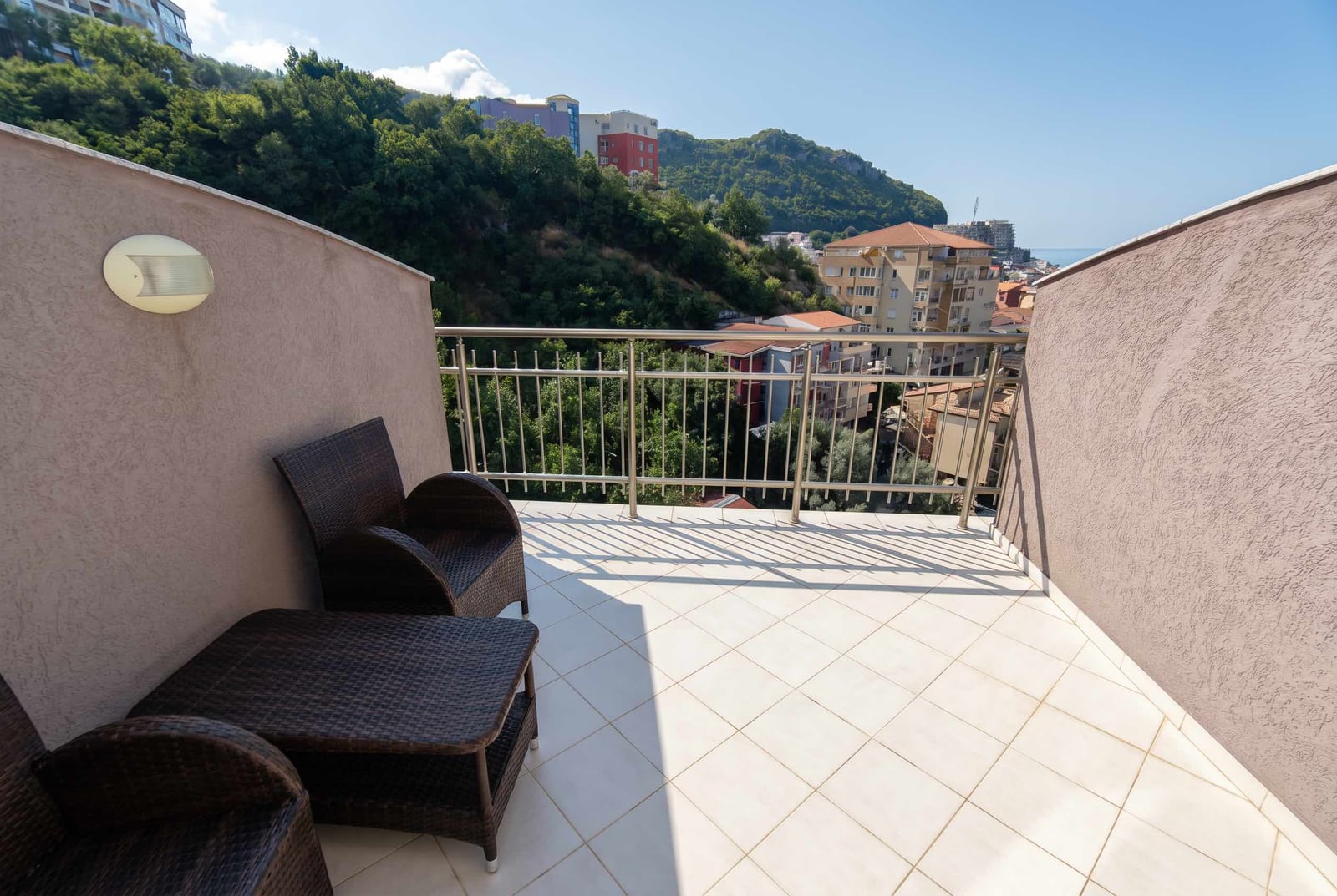 Terrace with wicker furniture and views of the mountains and the sea in an apartment, Becici, Montenegro. Light-colored tiles on the balcony floor.