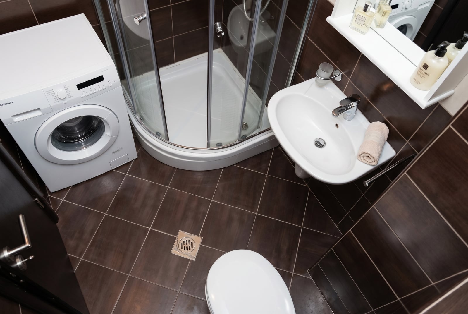 Bathroom in a Budva apartment, Montenegro: shower cabin, washing machine, and dark tile interior.