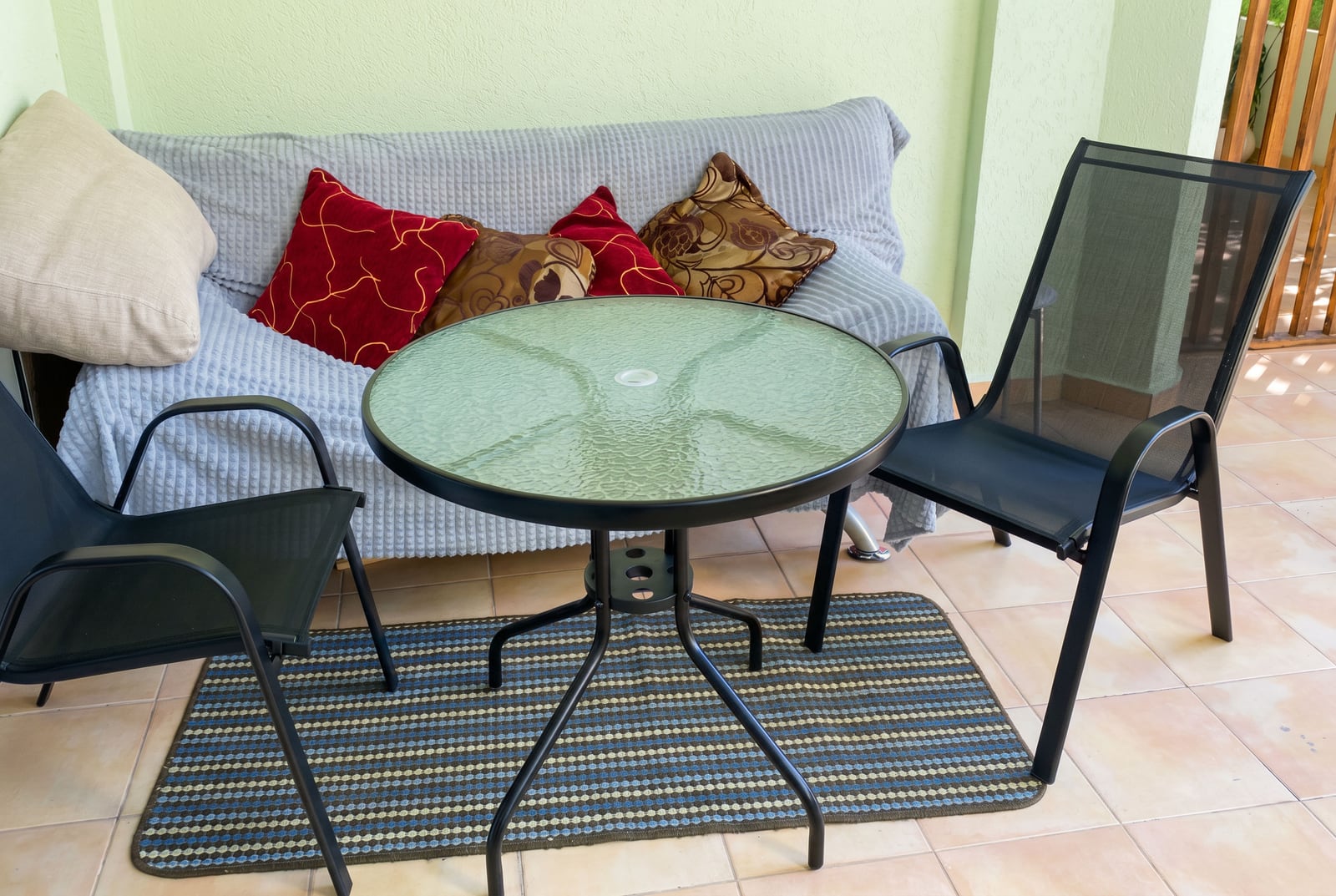 Cozy lounge area on a balcony of an apartment in Budva, Montenegro: a round table, two chairs, and a sofa with decorative pillows.
