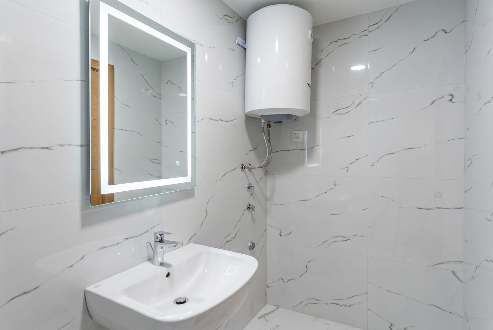 Modern bathroom in an apartment in Pržno, Montenegro: white marble-look tiles, illuminated mirror, and water heater.