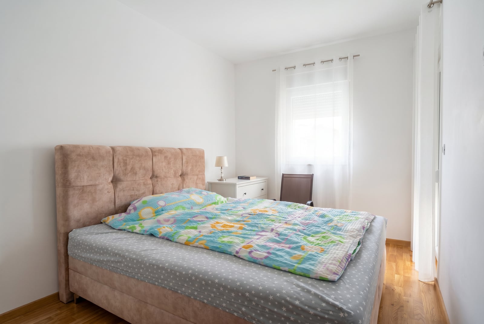 Bright bedroom with a double bed in an apartment in Bečići, Montenegro: parquet flooring, white walls, bedside table.