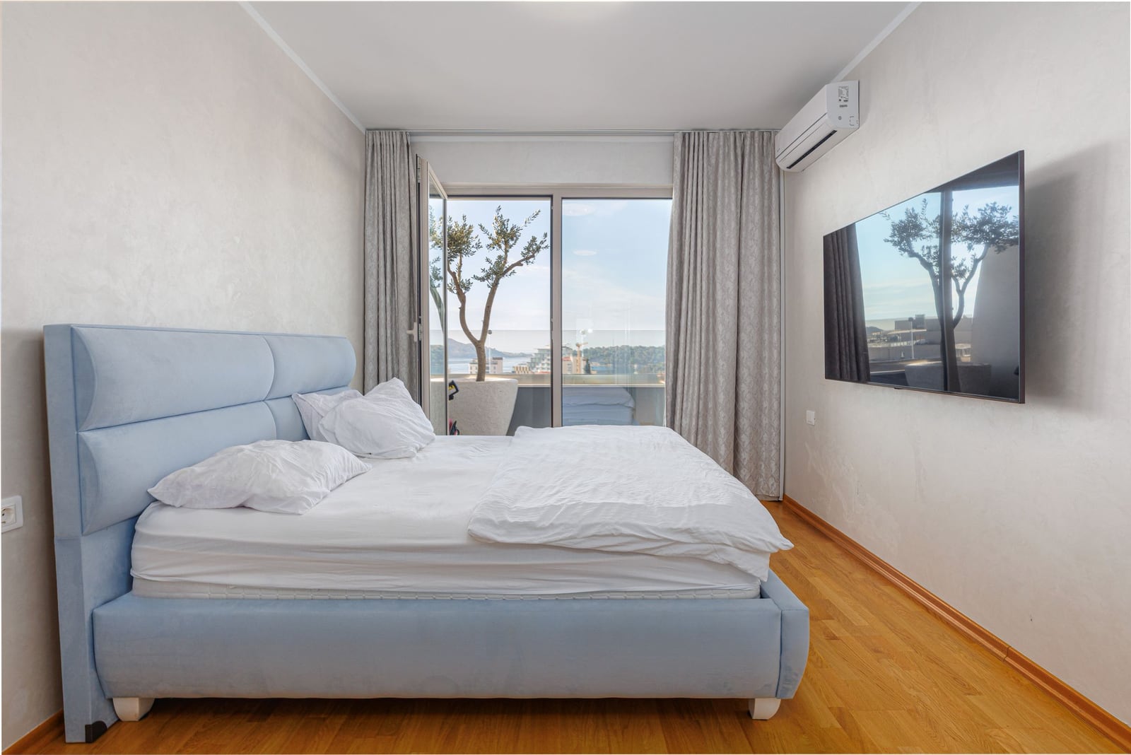 Bedroom in a penthouse in Becici, Montenegro: double bed, wall-mounted TV, and access to a terrace with a sea view.