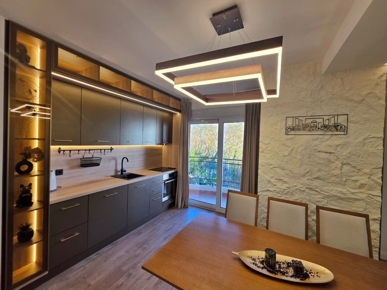 Modern kitchen in an apartment in Bečići, Montenegro: dark cabinetry, dining area, and access to a balcony with a view.