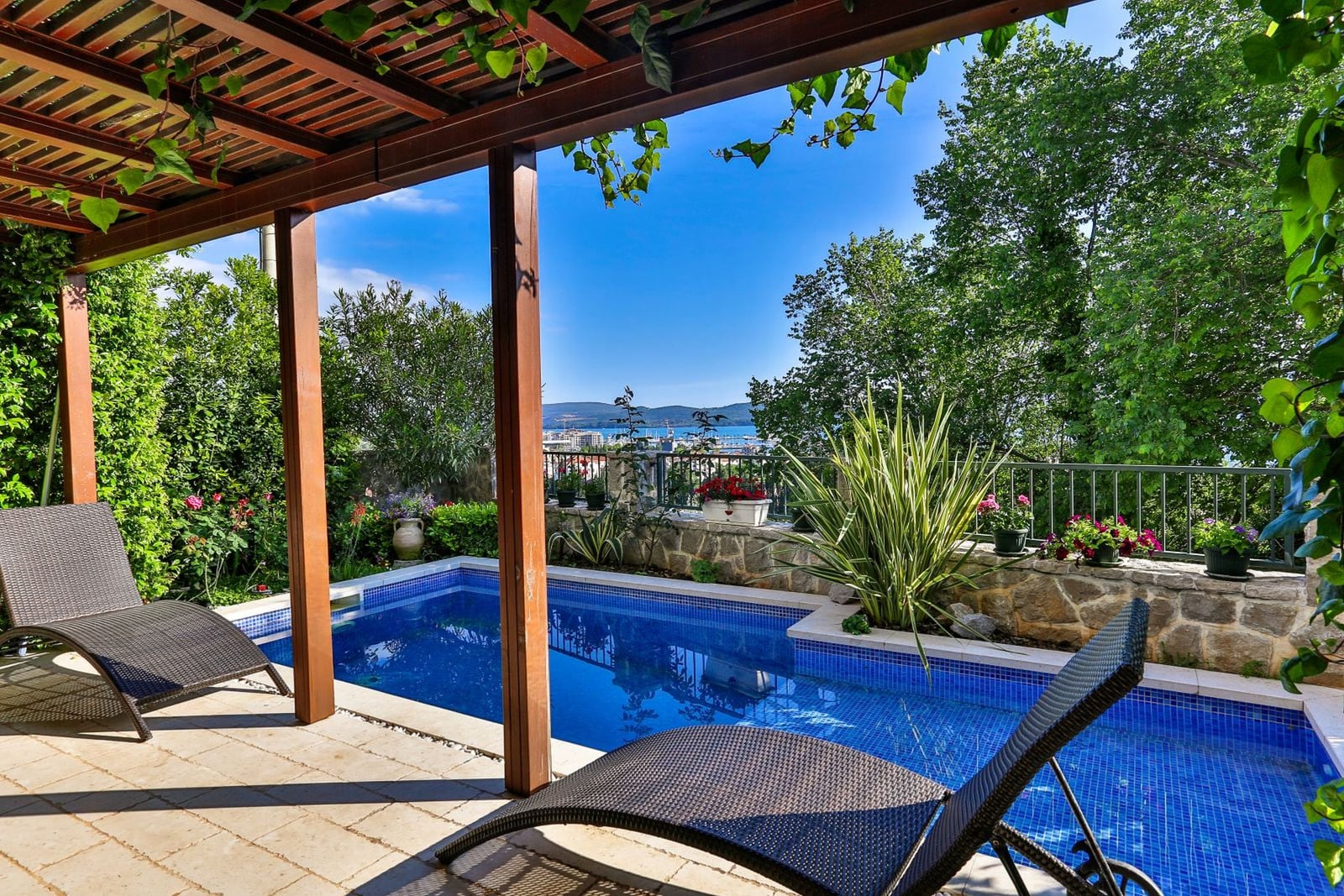 Terrace with a pool and sun loungers at a villa in Tivat, Montenegro, with panoramic views of the sea and green surroundings.