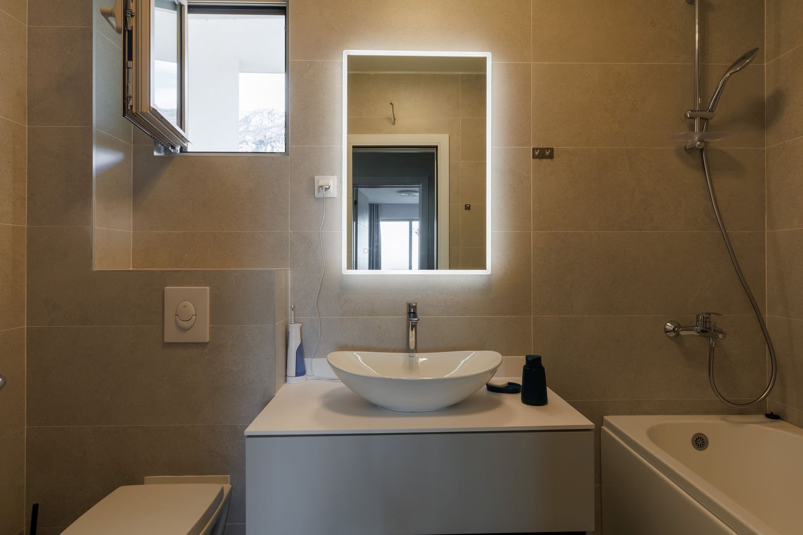 Modern bathroom in a penthouse in Becici, Montenegro: vessel sink, backlit mirror, and shower.