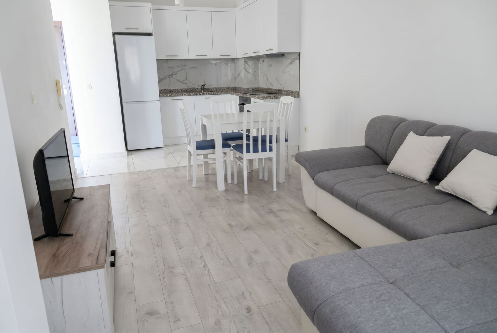 Modern living room with a sectional sofa, white kitchen, and dining area in an apartment in Budva, Montenegro