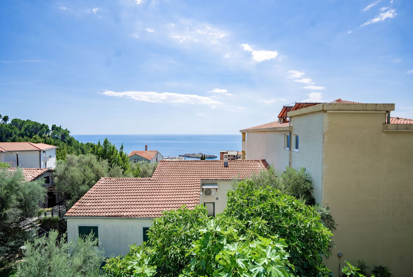 Panoramic view of the sea and tiled rooftops in Sveti Stefan, Montenegro, from the apartment terrace surrounded by greenery.