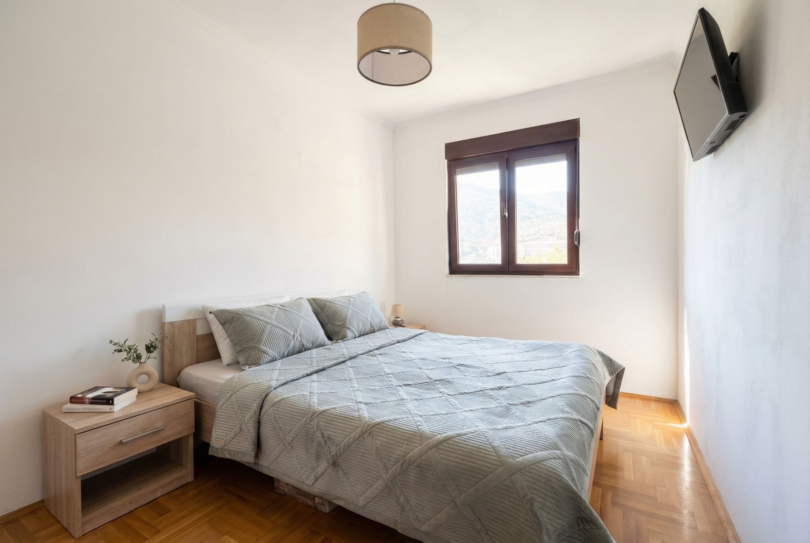 Bright bedroom with a double bed and parquet flooring in an apartment in Budva, Montenegro. View of the mountains from the window.