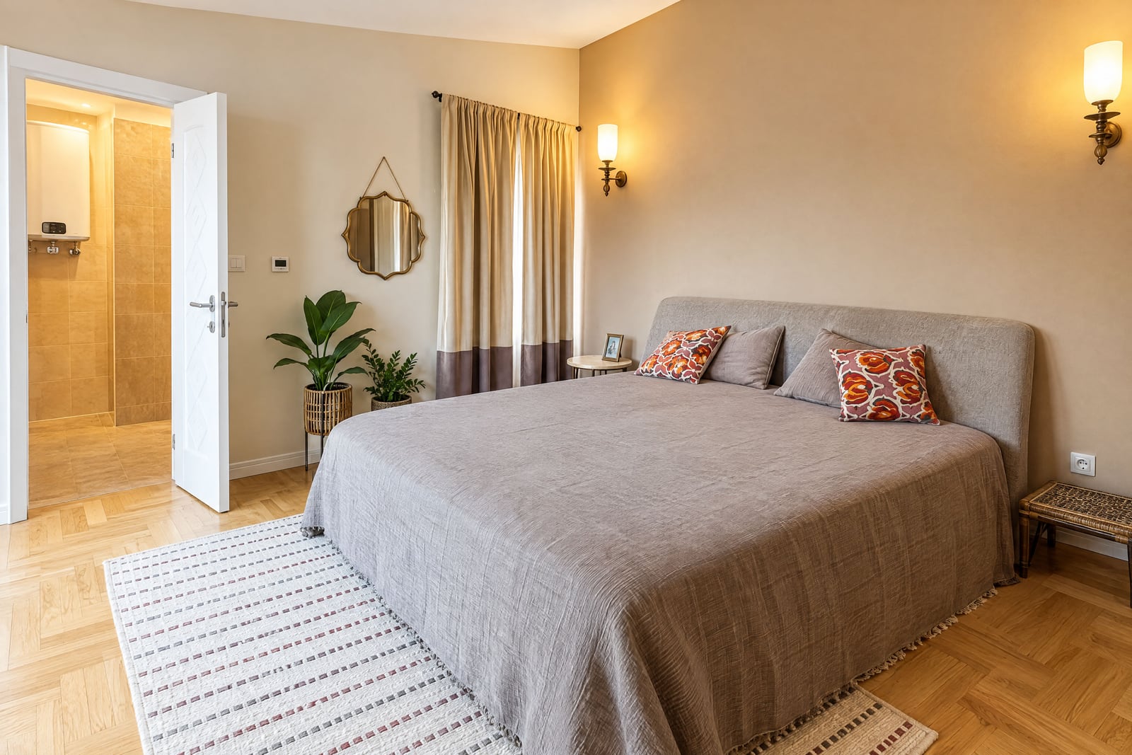 Bedroom featuring a large bed with grey coverlet, floral pillows, area rug, potted plant, and wall sconces.