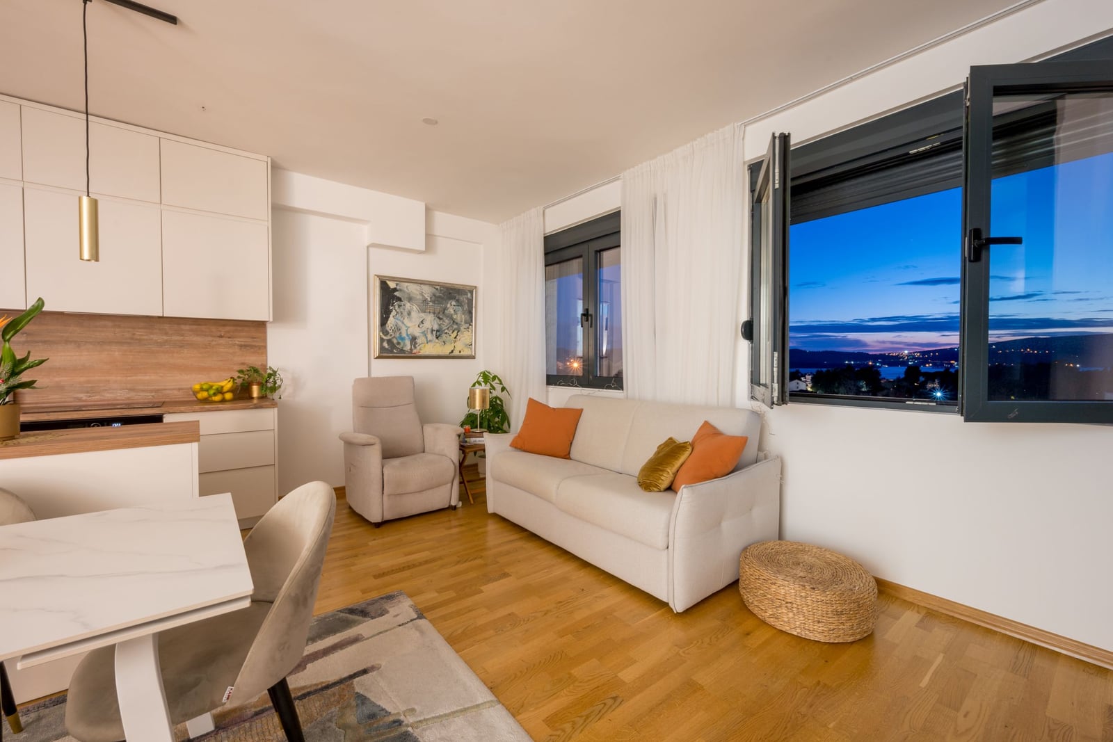 Modern living room with kitchen in an apartment in Tivat, Montenegro: light-colored furniture, parquet flooring, and panoramic sea views.