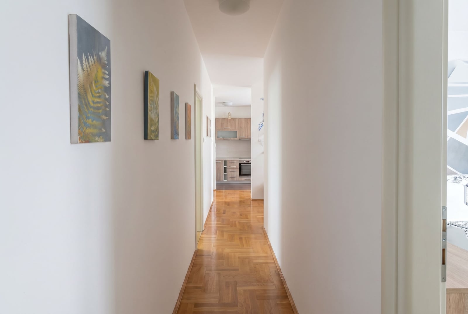 Bright hallway with parquet flooring and paintings in an apartment in Bečići, Budva, Montenegro, view of the kitchen area.