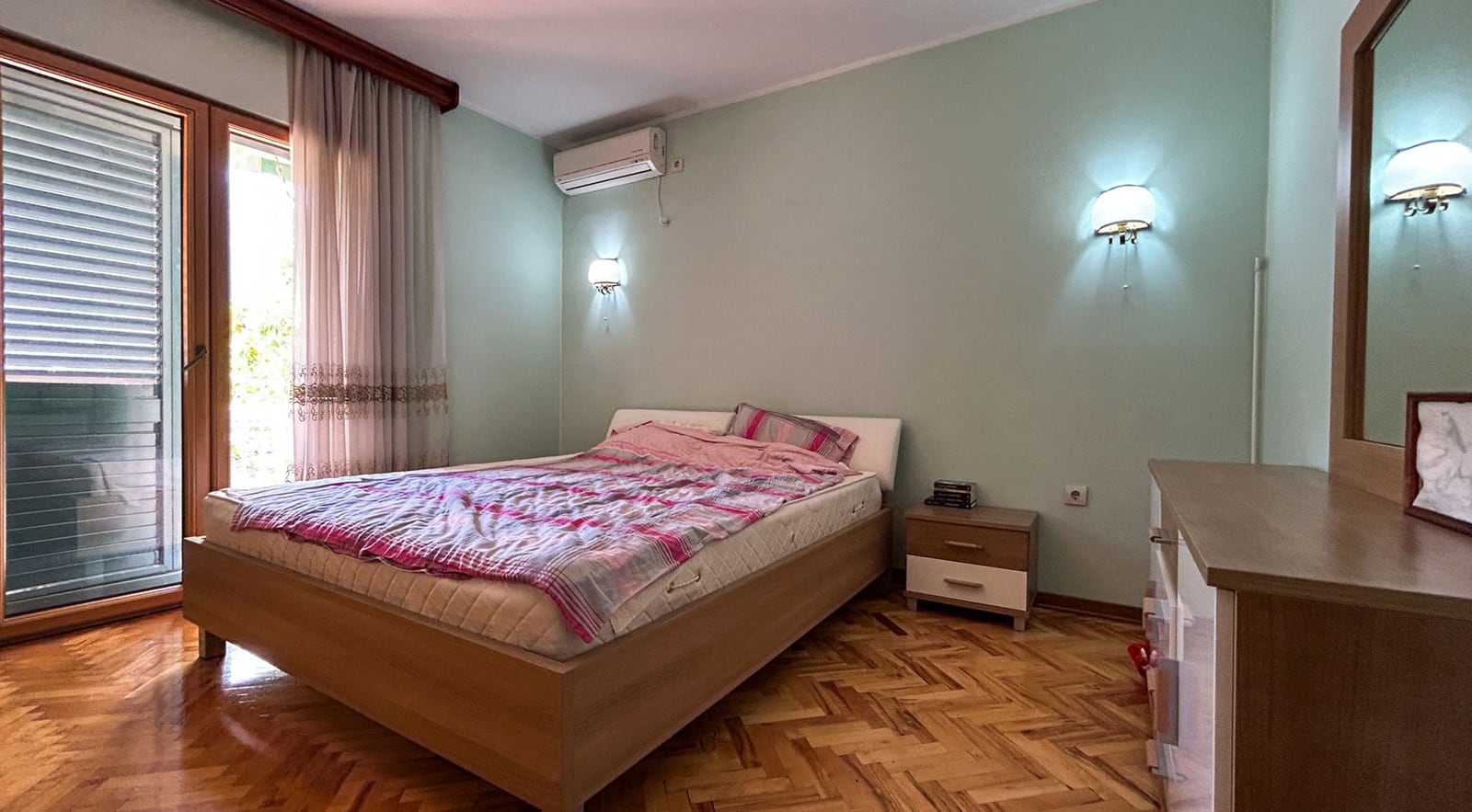 Bedroom with a double bed and parquet flooring in a villa in Dobrota, Montenegro: view of the terrace and wooden furniture.