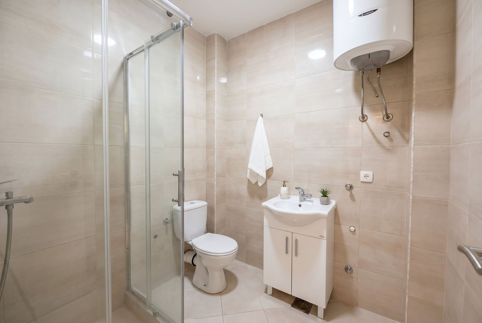 Modern bathroom in a Budva apartment, Montenegro: walk-in shower, white sanitary ware, and beige tiling.