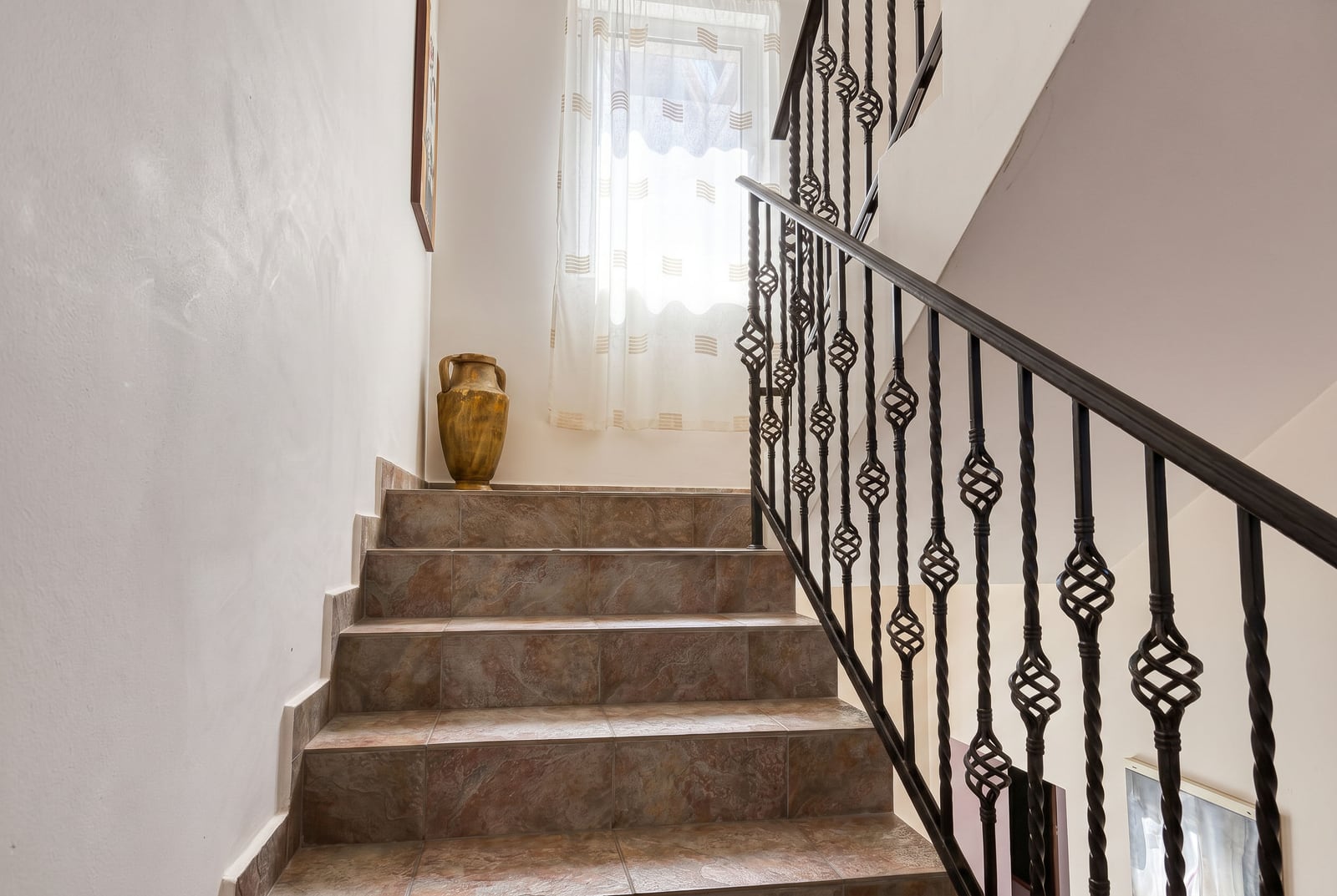 Staircase with wrought iron railings and ceramic tiles in a villa in Bečići, Montenegro. Home interior with a decorative vase.