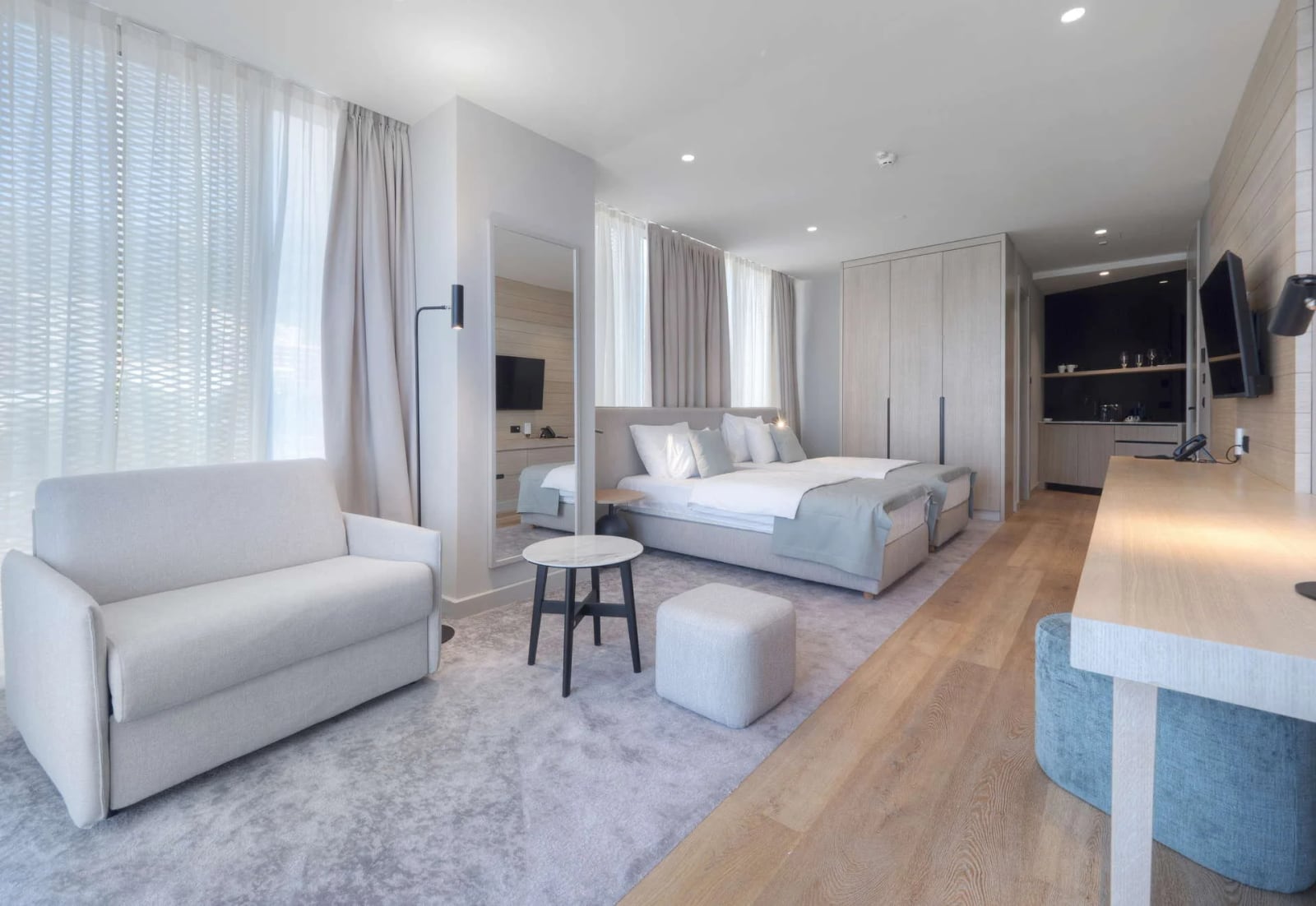 Modern studio room combining a sleeping area, lounge with sofa, and kitchenette in one open space.