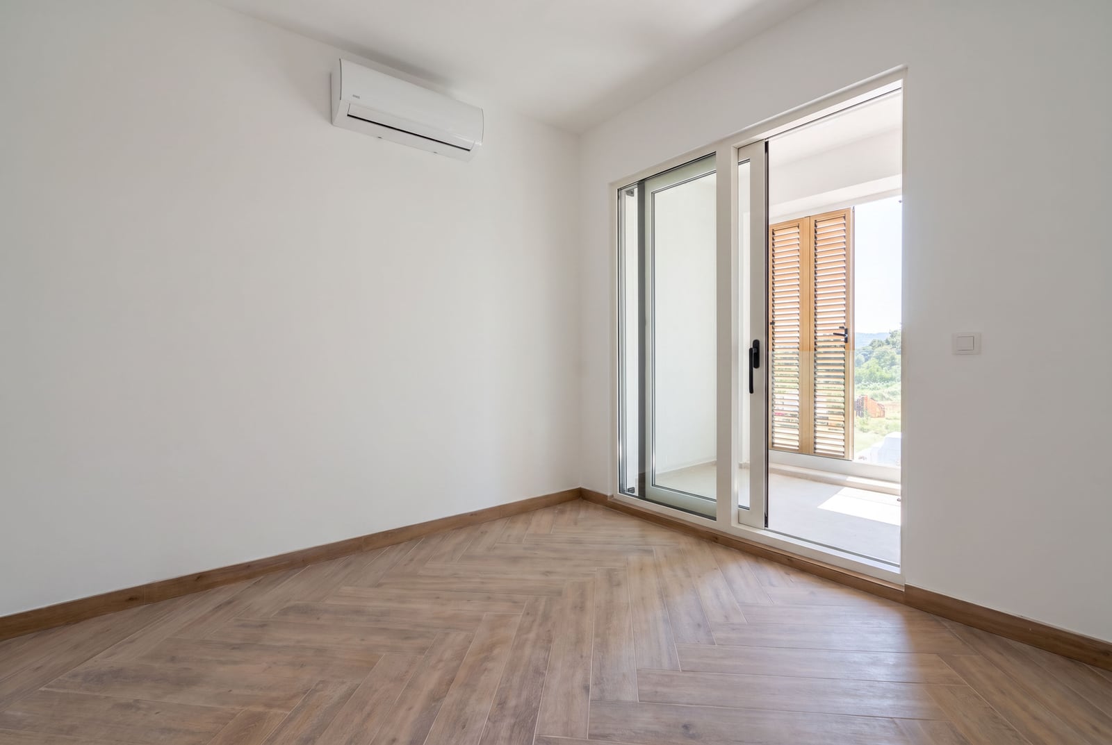 Bright bedroom with herringbone parquet flooring and balcony access in an apartment in Tivat, Montenegro.