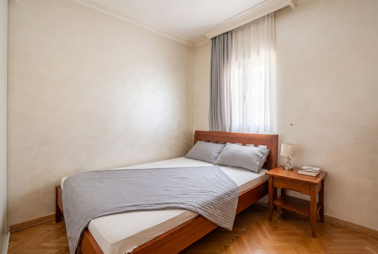 Cozy bedroom with a wooden bed and parquet flooring in an apartment for sale, Budva, Montenegro.