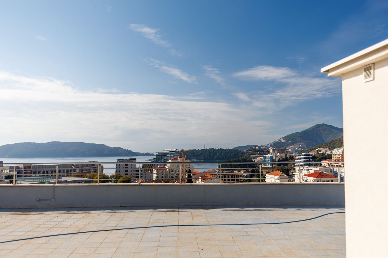 Panoramic view of the sea and mountains from the open terrace of a penthouse in Bečići, Montenegro, with a metal railing.