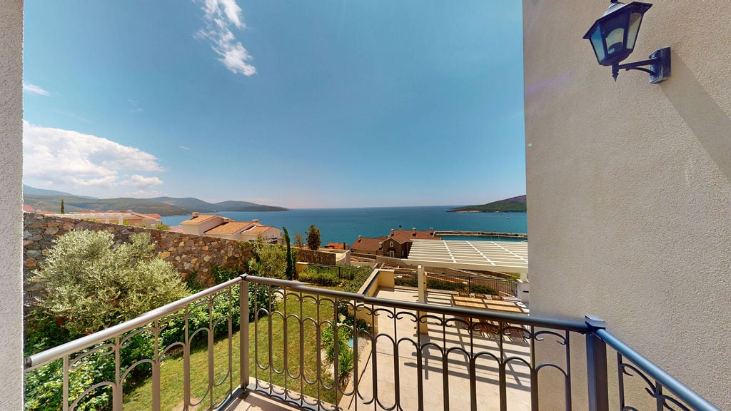 View from the balcony of a villa in Luštica, Montenegro: a panorama of the sea, mountains, a terrace with garden furniture, and a well-maintained garden.