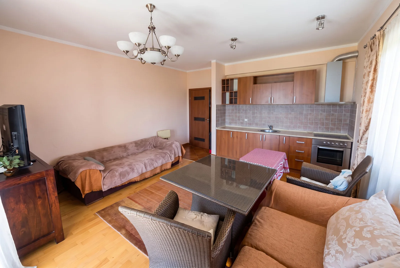 Living room with kitchen area featuring sofas, dining table, TV, and wooden cabinetry.