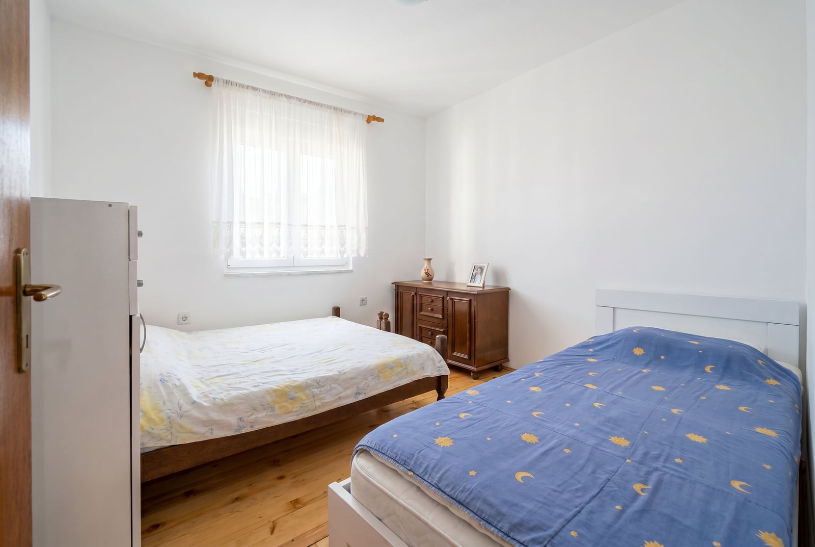 Bright bedroom with two beds, a wooden dresser, and parquet flooring in a house for sale in Sutomore, Montenegro.
