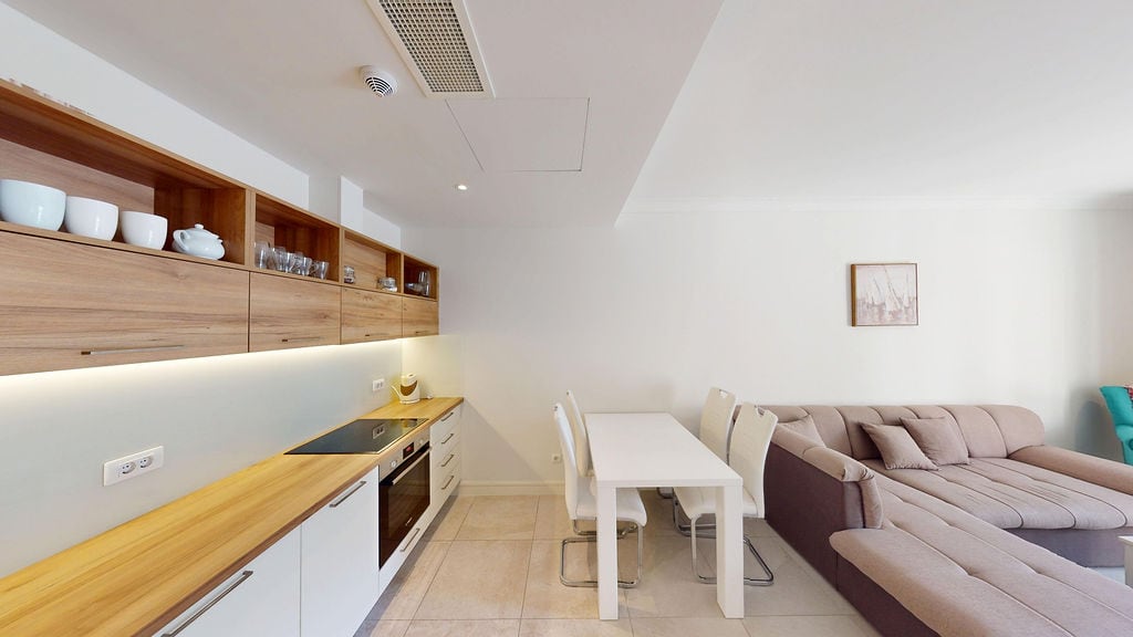 Modern kitchen-living room with wooden facades in an apartment, Luštica, Montenegro: dining area and soft sofa.