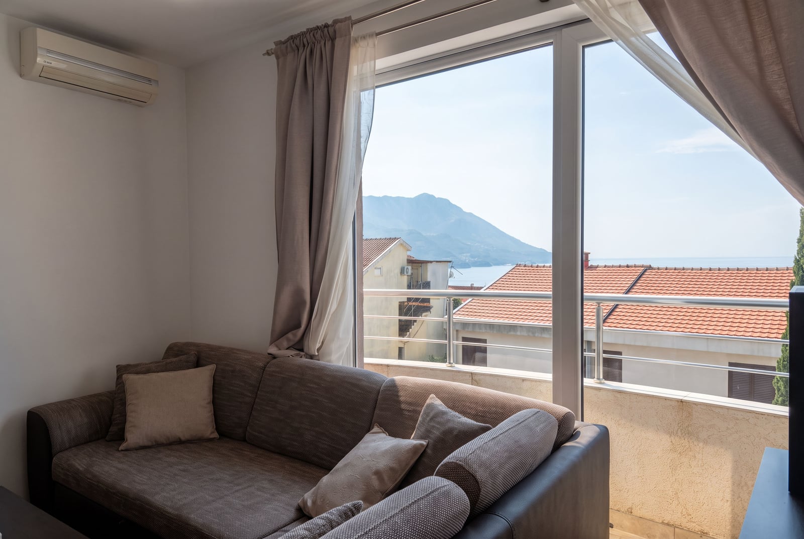 Living room with a soft sofa and panoramic window overlooking the sea and mountains in Bečići, Montenegro