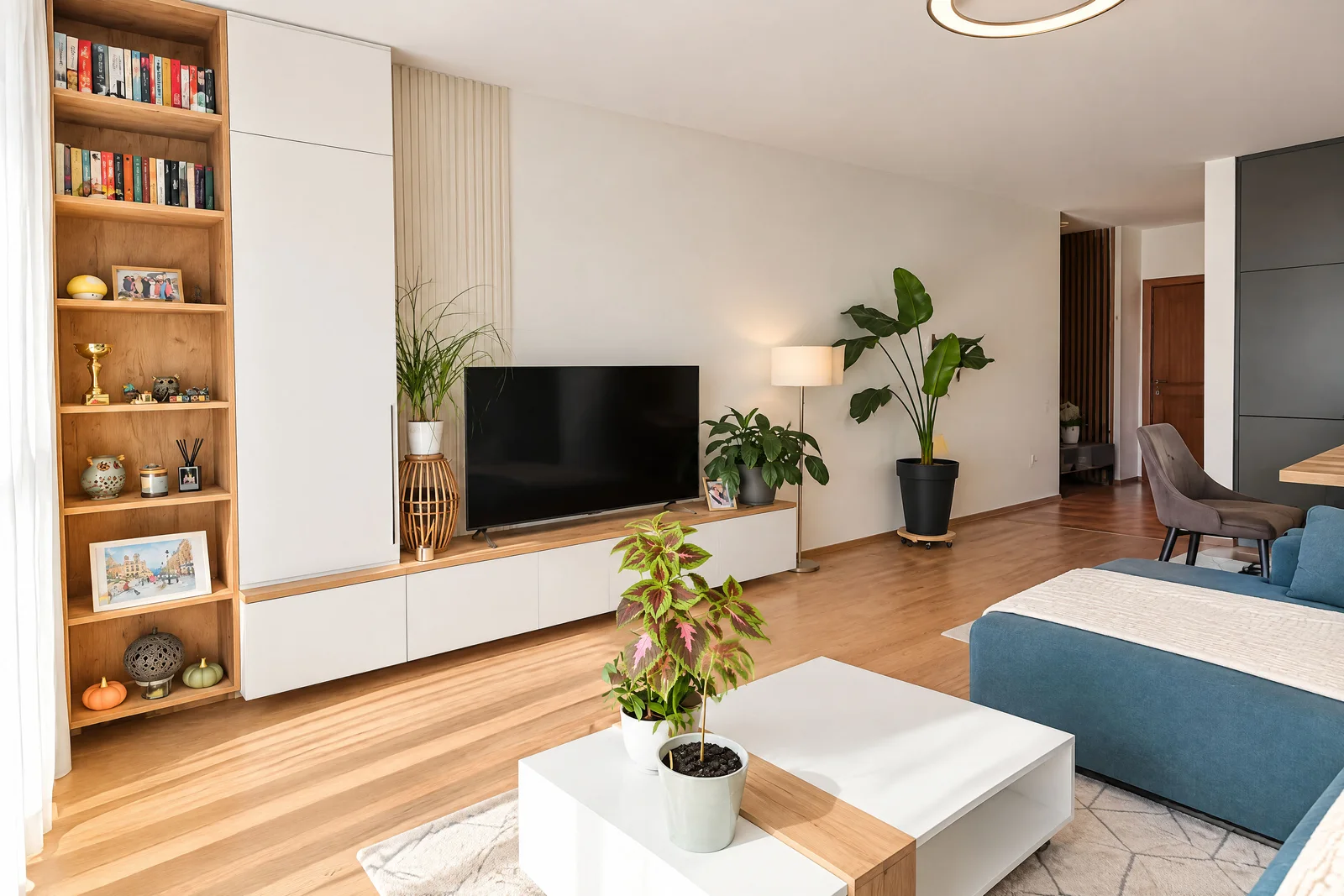 Modern living room featuring a blue sofa, white coffee table, TV unit, and tall wooden bookshelf with decor.