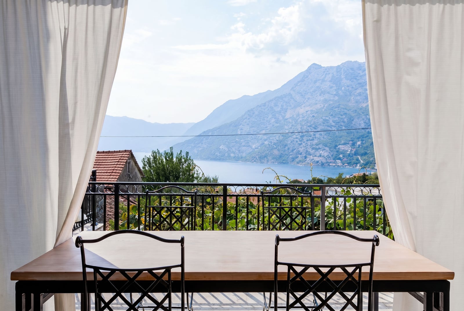 View from the balcony of an apartment in Risan, Montenegro: dining table, wrought iron chairs, and a panorama of the Bay of Kotor and the mountains.