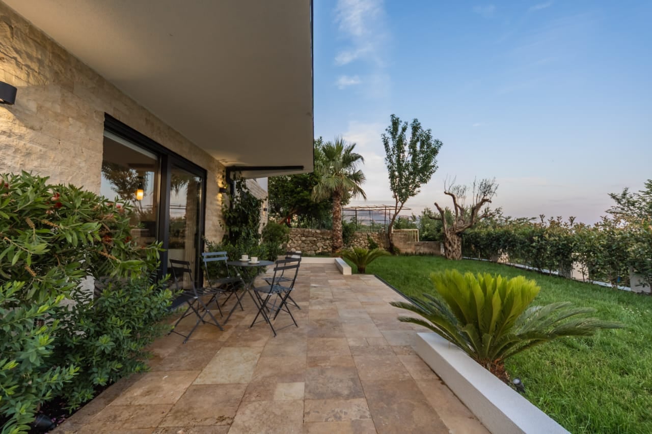 Villa terrace in Budva, Montenegro: stone finishing, garden furniture, and a well-maintained green plot with palm trees.