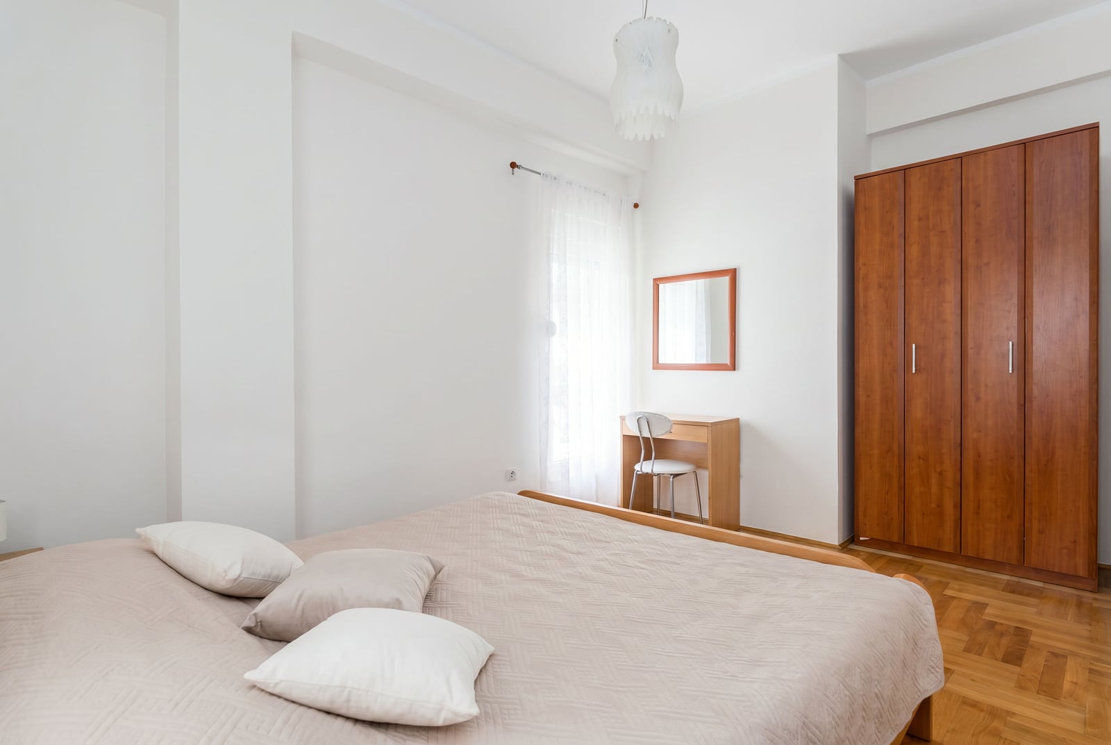 Bright bedroom in an apartment in Budva, Montenegro: double bed, wooden wardrobe, vanity table, and parquet flooring.