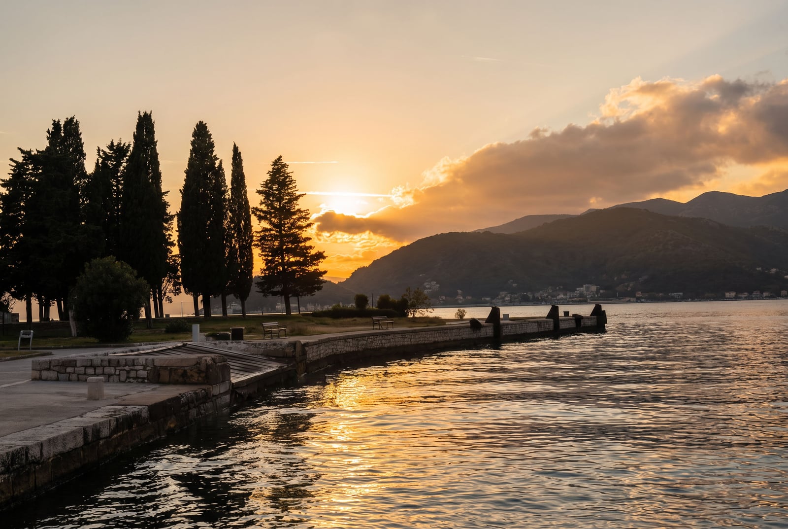Picturesque sunset view by the sea, the promenade with cypresses, and the mountains in Tivat, Montenegro.