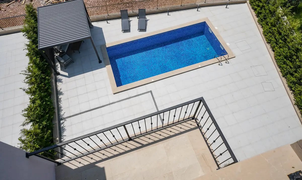 Private swimming pool with a terrace and lounge area at a villa in Reževići, Montenegro: top-down view of sun loungers and a canopy.