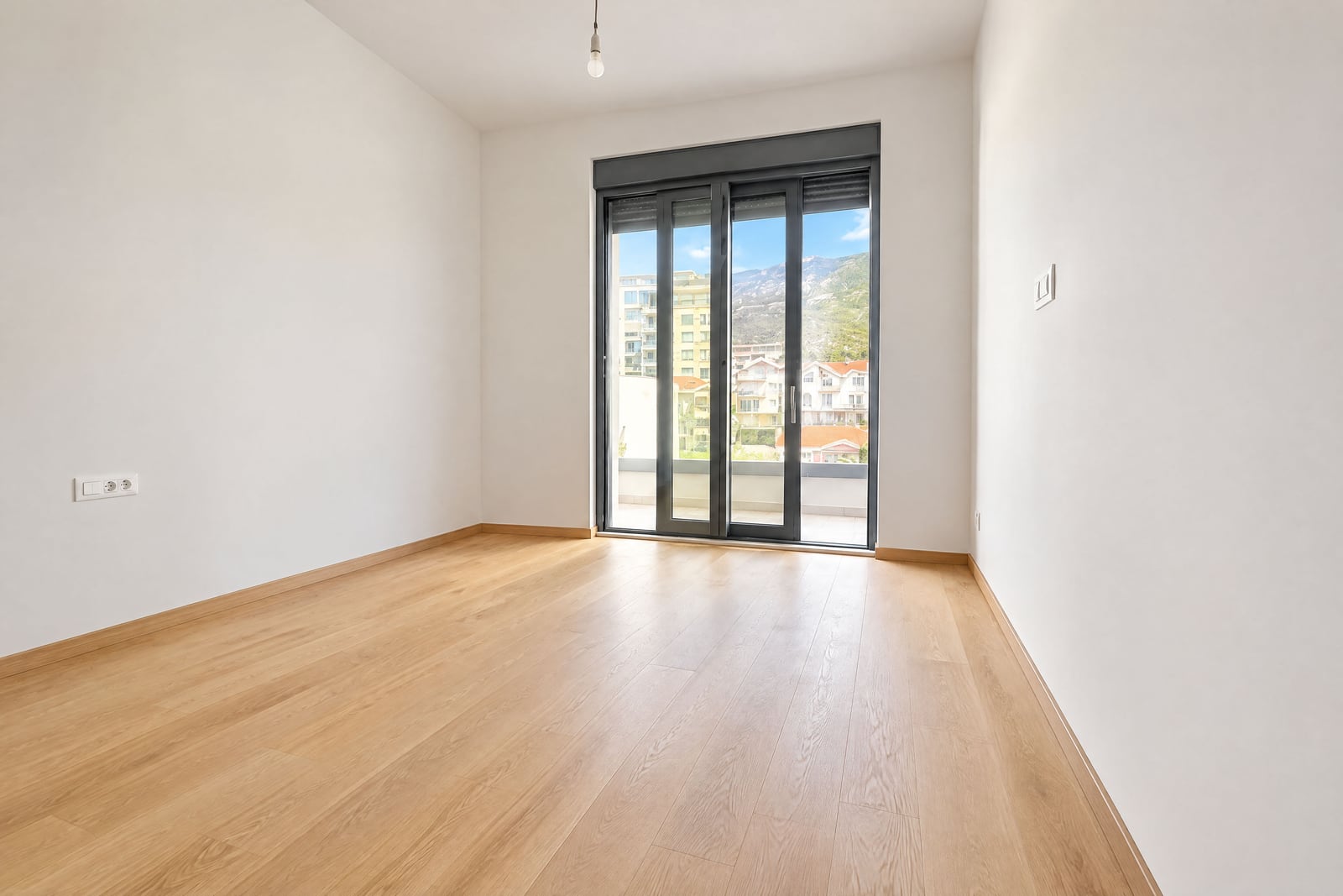 Empty room with light wood flooring and large sliding glass doors leading to a balcony with mountain views.
