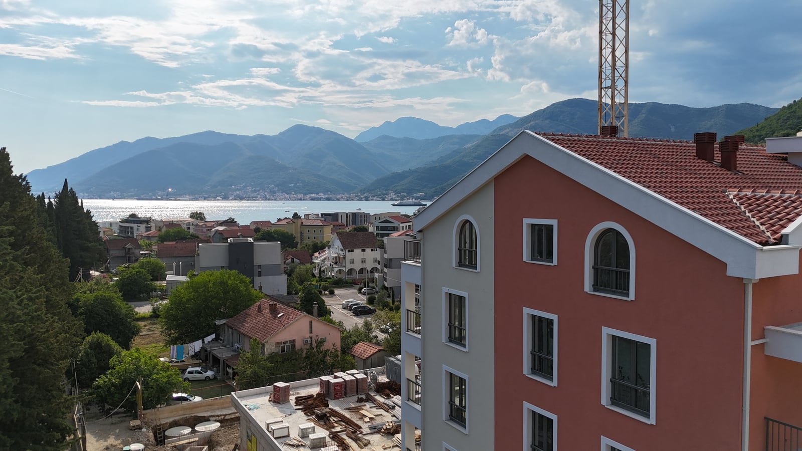View of the sea and mountains from a apartment window in Tivat, Montenegro: modern residential building with a tiled roof and a panoramic view of the city.