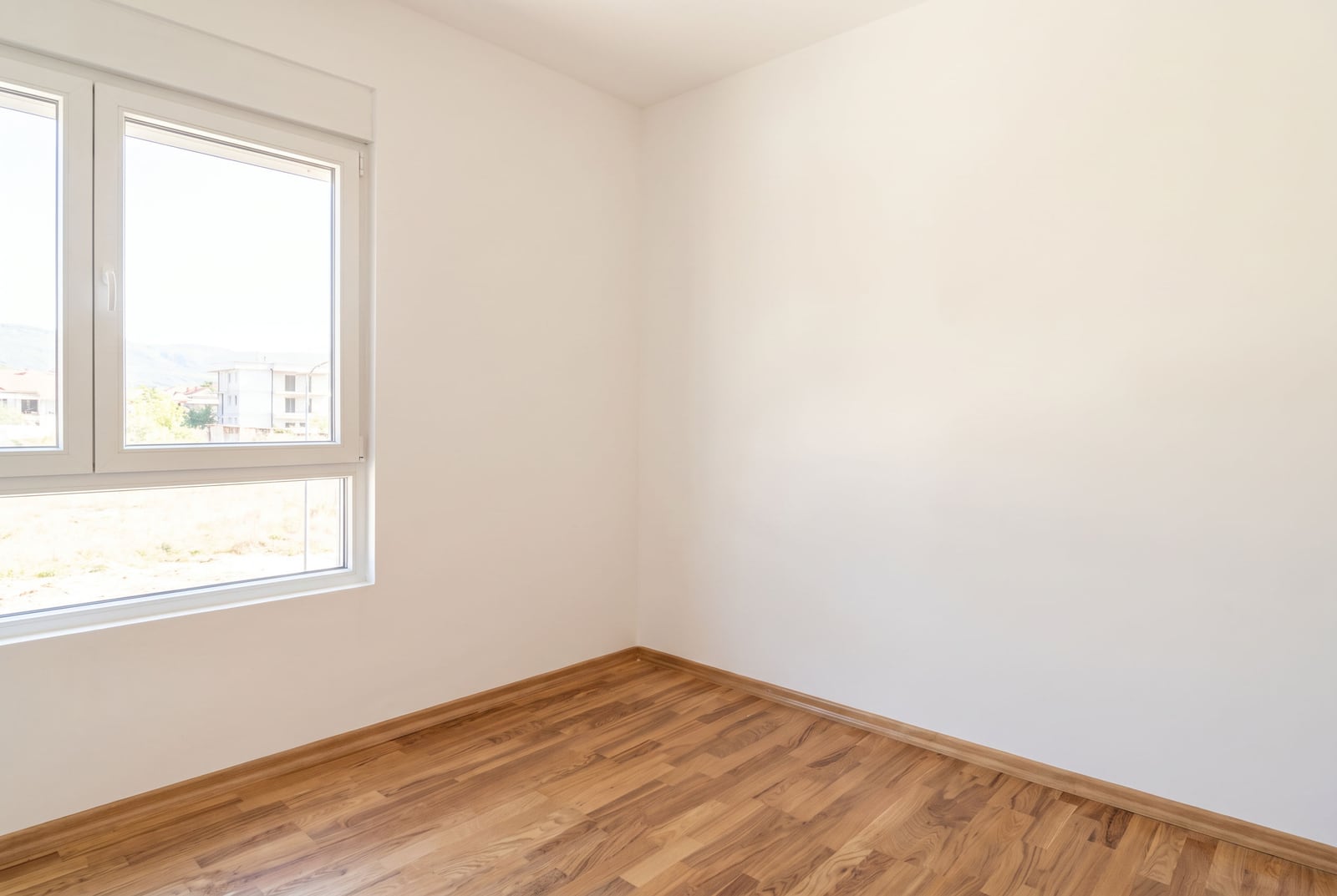 Bright empty bedroom with white walls, laminate flooring, and a window in an apartment in Budva, Montenegro