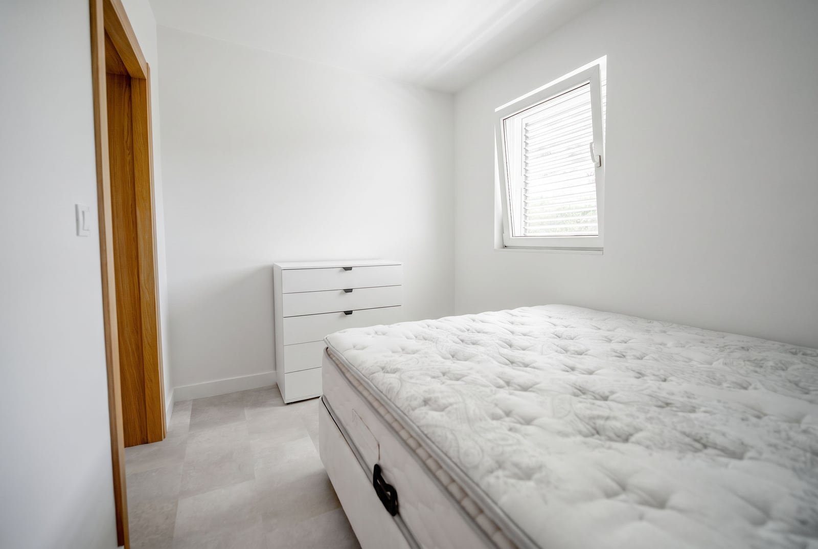 Bright bedroom with a white bed and dresser in an apartment in Sveti Stefan, Montenegro: modern interior with a window.