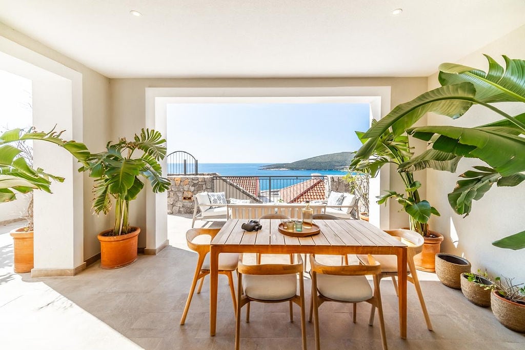 Terrace with dining area and sea view in the Luštica residential complex, Montenegro: wooden table, potted plants.