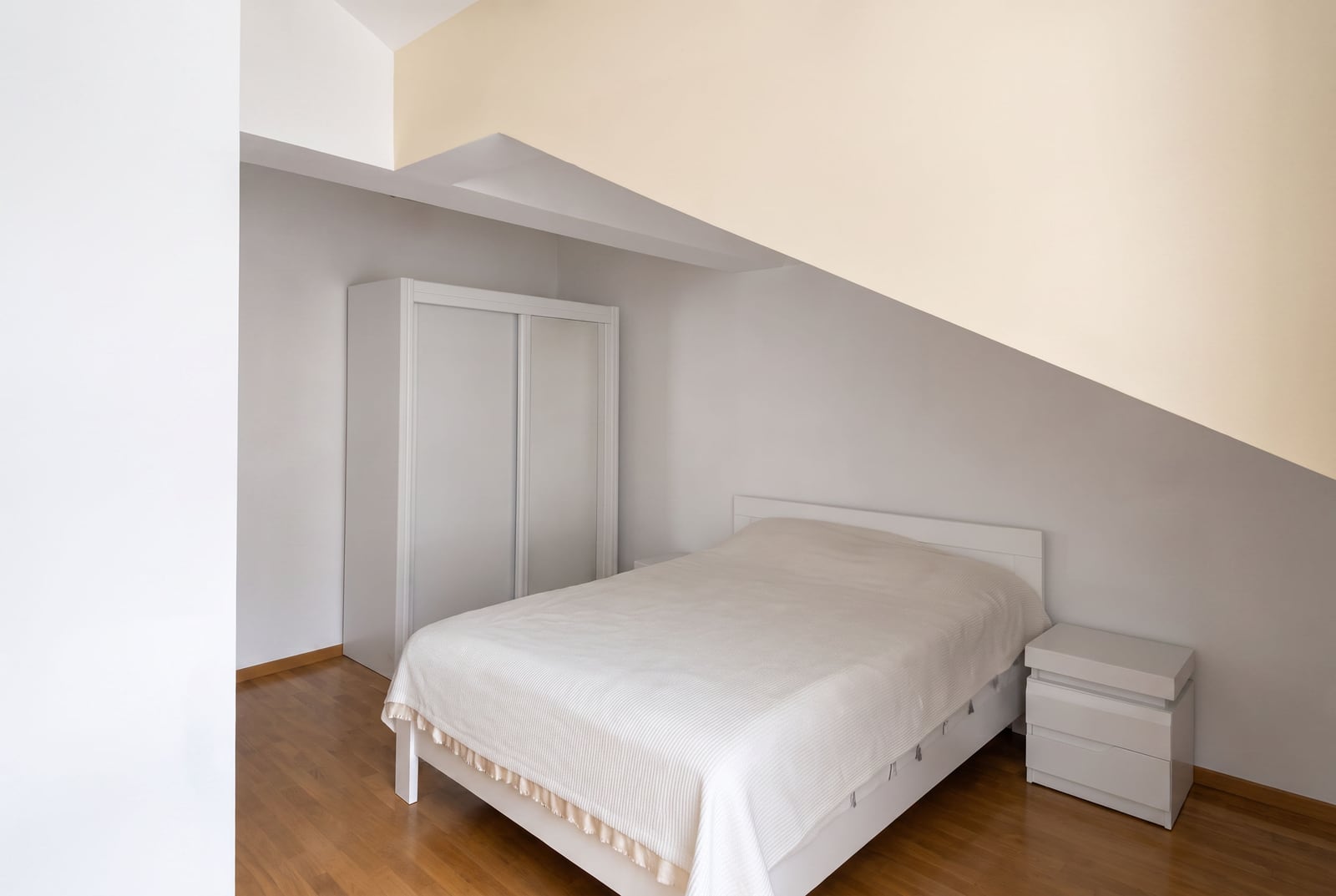 Bedroom featuring a white bed, sliding wardrobe, and nightstand on wooden flooring under a sloped ceiling.