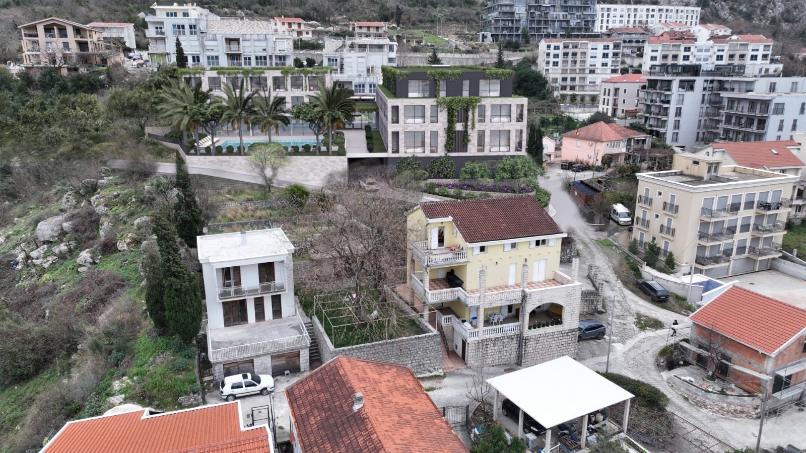 Aerial view of a residential area featuring houses, a pool, and palm trees on a hillside.