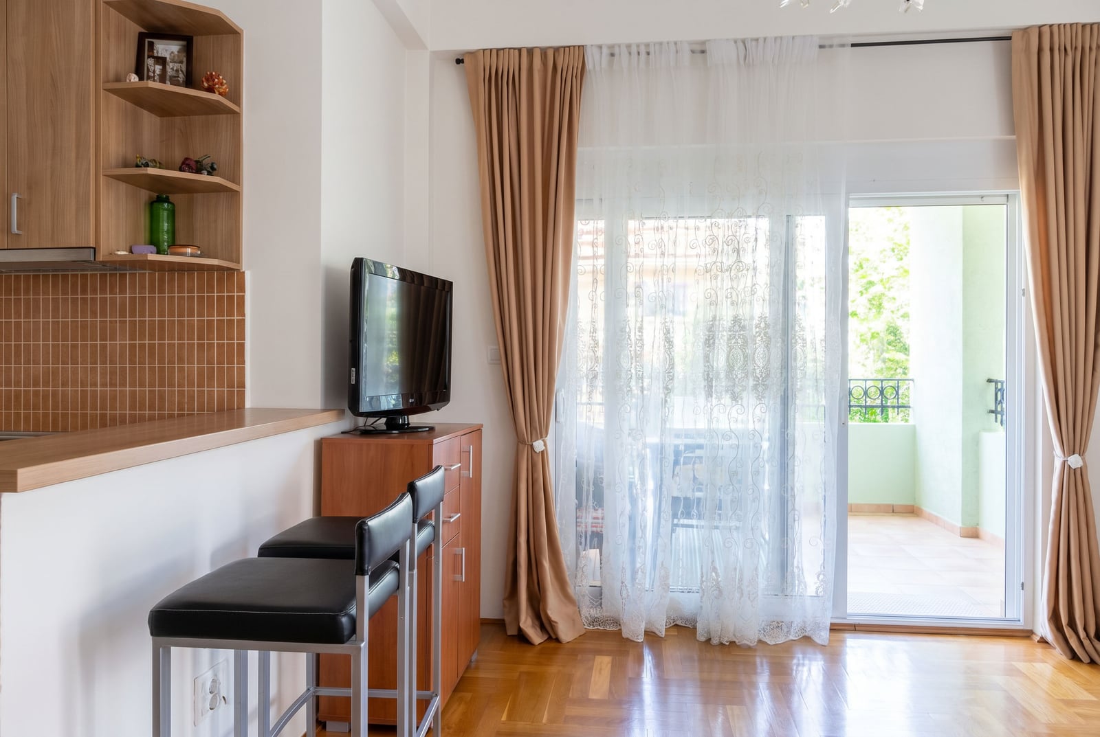 Living room with a breakfast bar and balcony access in an apartment in Budva, Montenegro. Parquet flooring, TV, and bright interior.