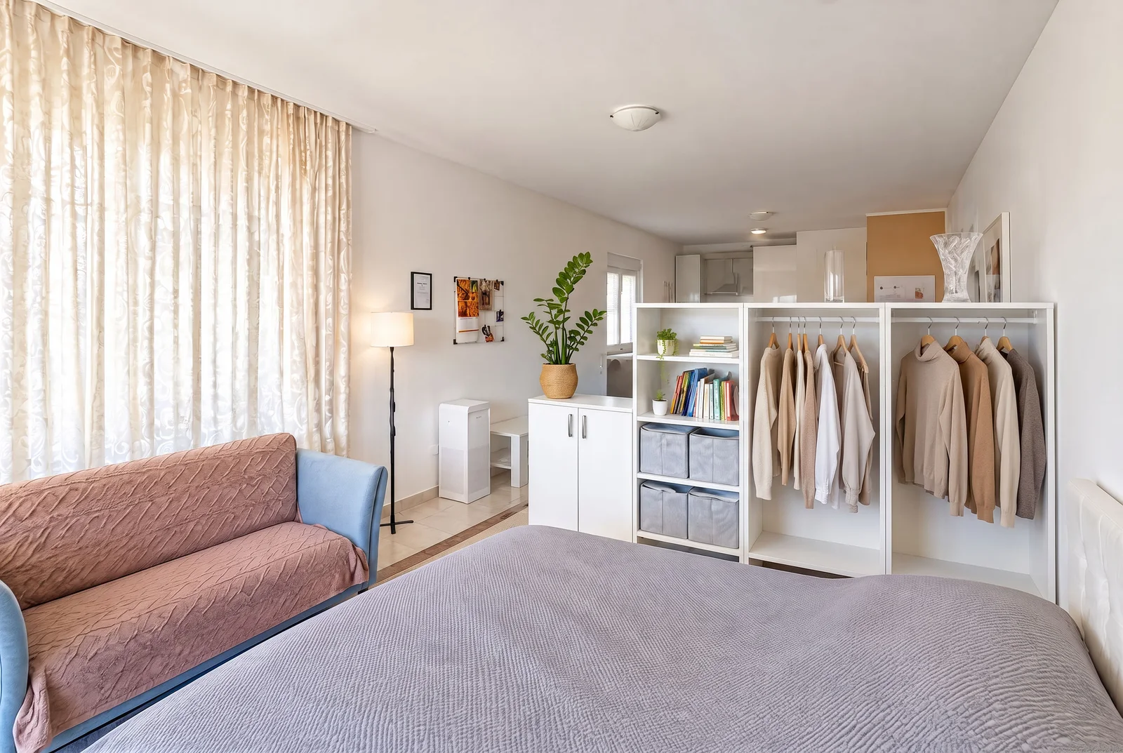 Bedroom featuring a large bed, open clothing rack with garments, and a sofa near the window.
