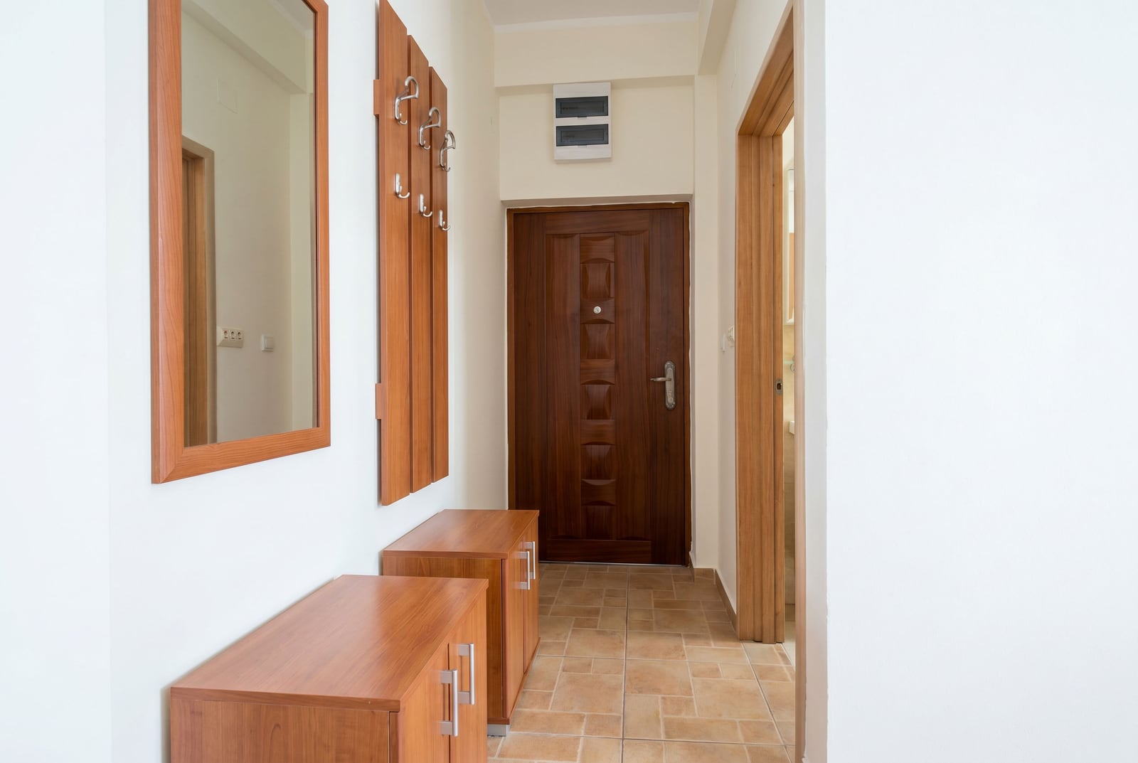 Bright hallway in a Budva apartment, Montenegro: wooden furniture, mirror, entrance door, and tiled floor.