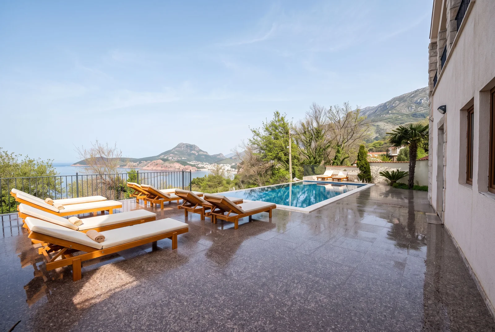 Outdoor pool terrace with wooden loungers overlooking the sea and mountains.