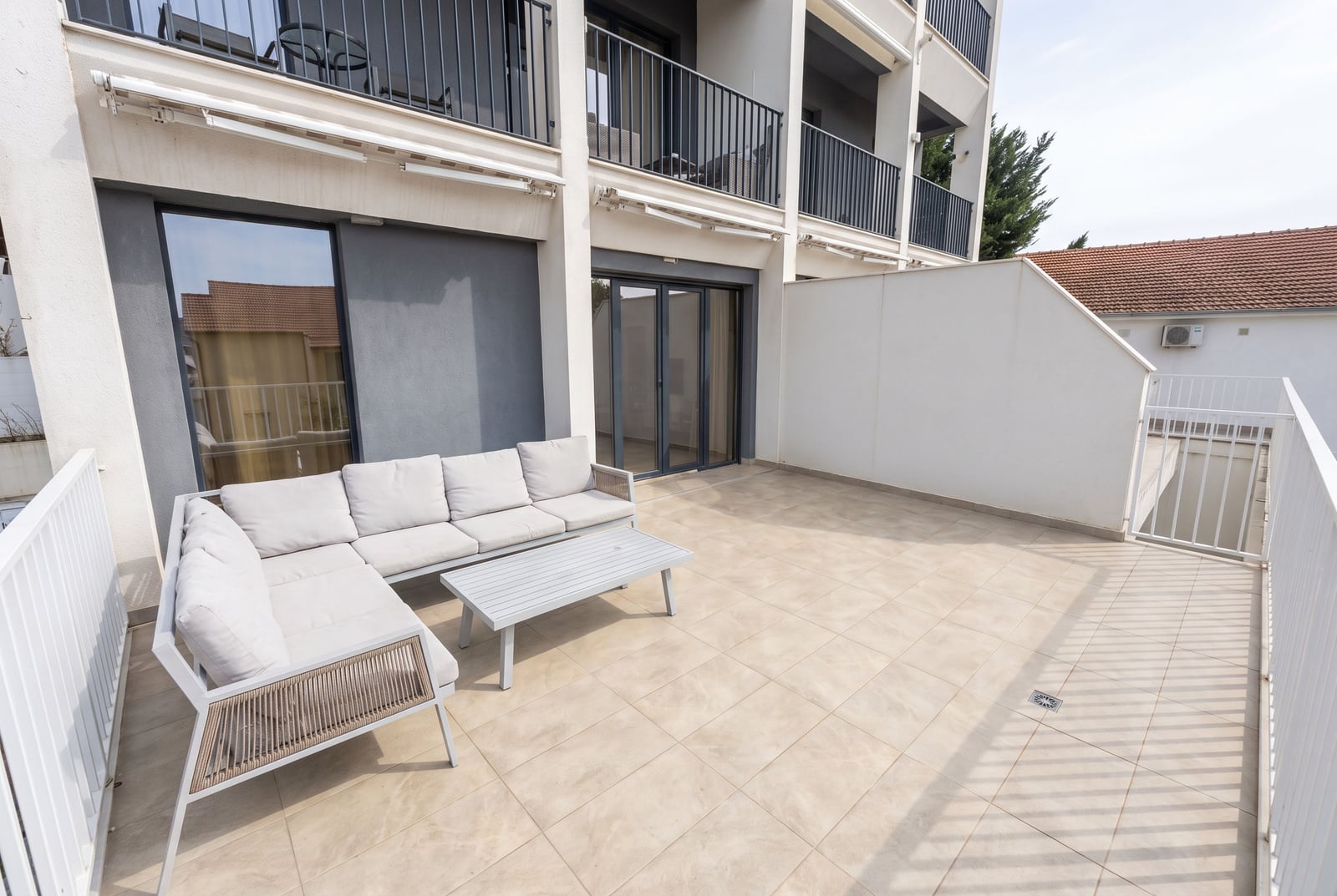 Wide open balcony with white outdoor furniture and tiled floor, enclosed by a white railing.