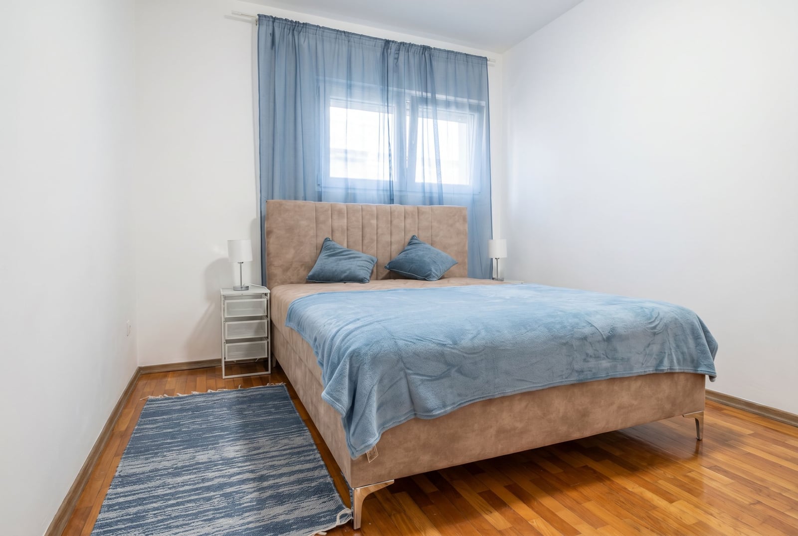 Cozy bedroom with a double bed in an apartment, Budva, Montenegro: parquet floor, blue textiles, and a bright interior.