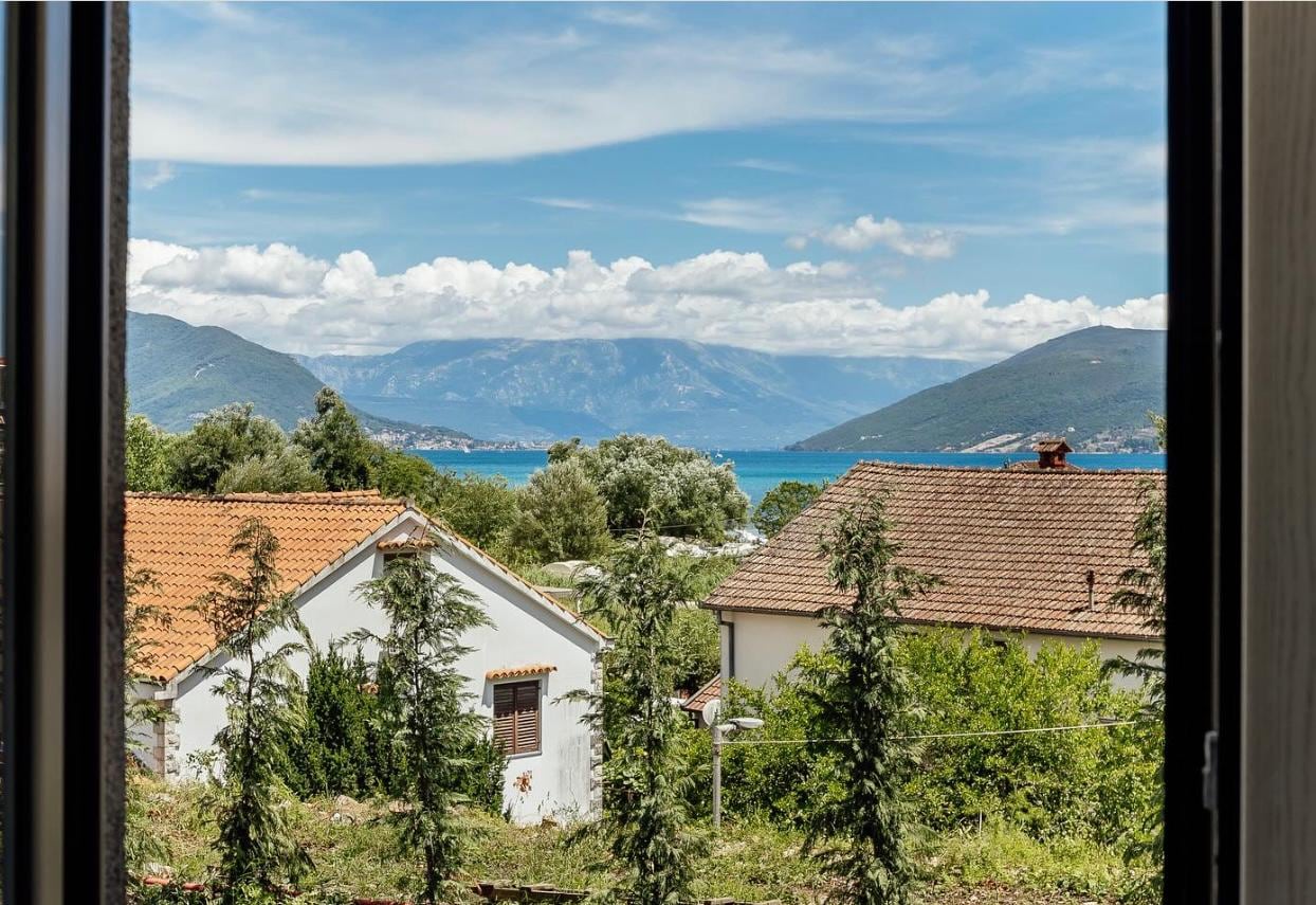 View from the apartment window in Igalo, Montenegro: a picturesque landscape of the sea, mountains, and tiled rooftops.