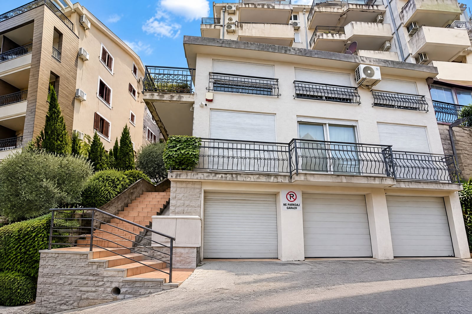 Exterior view of a building facade featuring garages, balconies, and outdoor stairs.